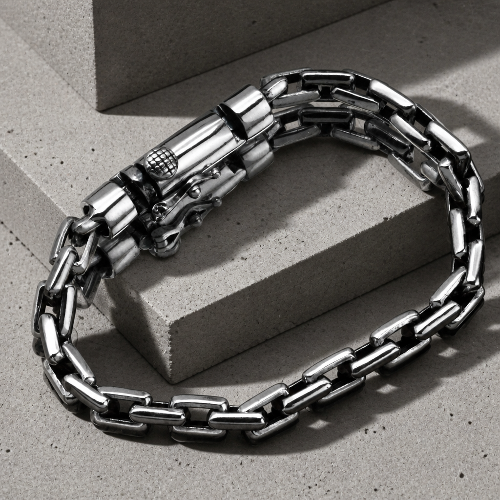 Bracelet chaîne argent homme posé sur du béton, maille carrée ajourée et fermoir barillet