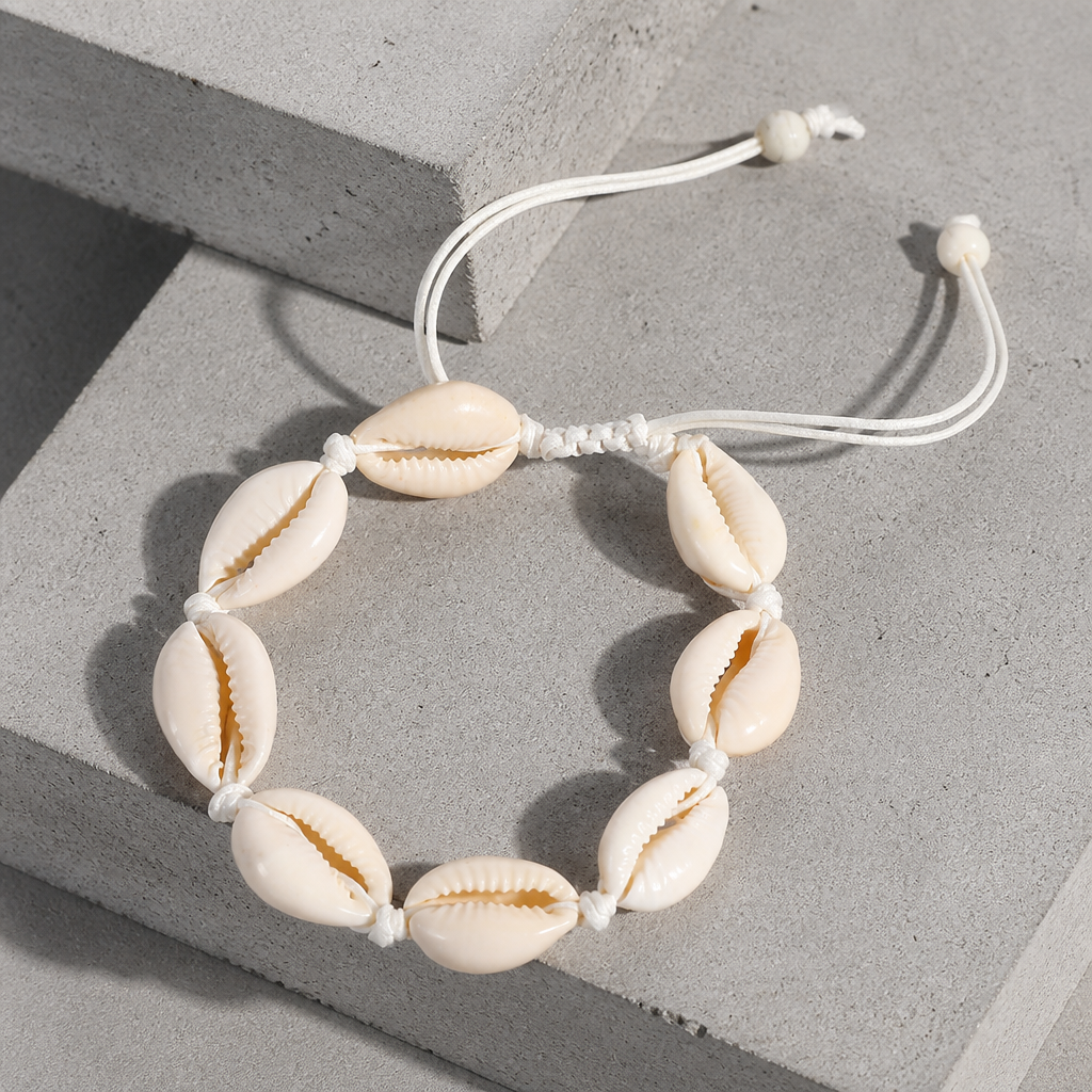 Bracelet coquillage homme, rang de cauris sur cordon blanc, posé sur un bloc de béton