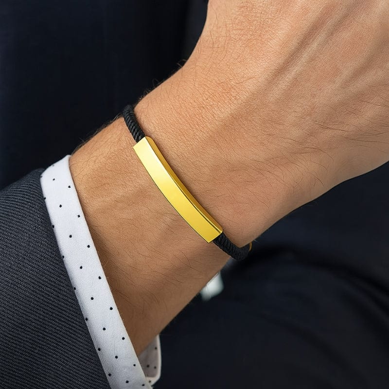 Bracelet homme à graver porté au poignet, cordon noir et barrette dorée