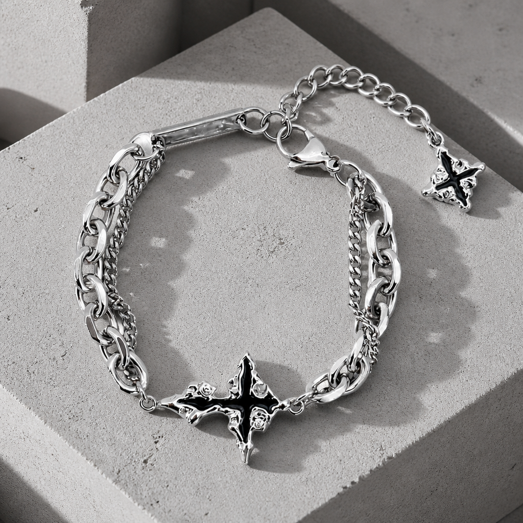 Bracelet croix homme argent posé à plat sur du béton, double chaîne en acier et croix centrale