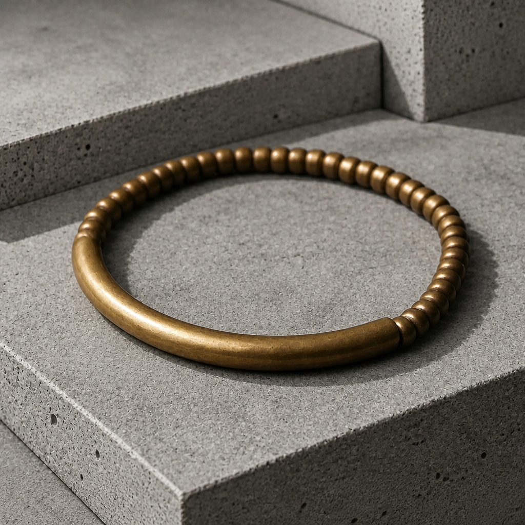 Bracelet homme doré en laiton patiné, perles plates et tube lisse, posé sur du béton