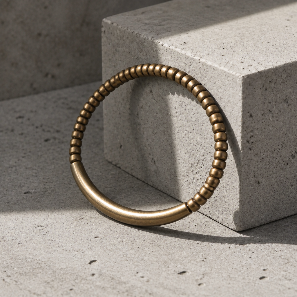 Bracelet en laiton doré vu de trois quarts, appuyé contre un bloc de béton