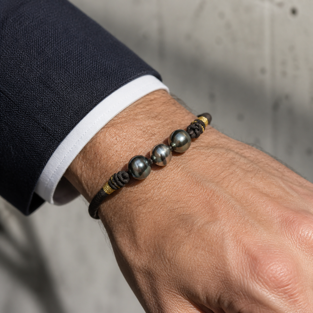 Bracelet trois perles de Tahiti porté au poignet d'un homme, cordon brun et doré