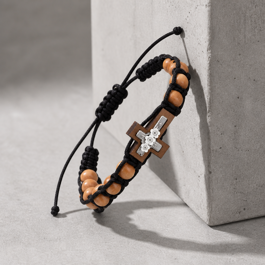 Bracelet perle croix homme, cordon noir tressé et croix encadrée, posé contre un bloc de béton