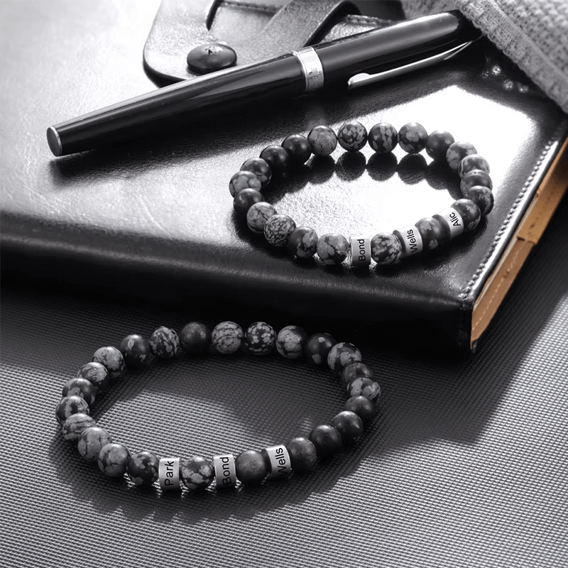 Deux bracelets homme en perles gravées posés près d'un stylo