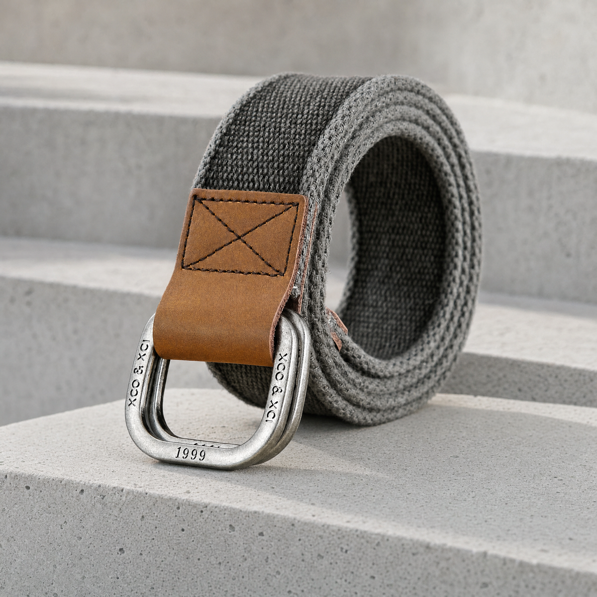 Ceinture en toile homme grise à double anneau gravé, posée sur un bloc de béton