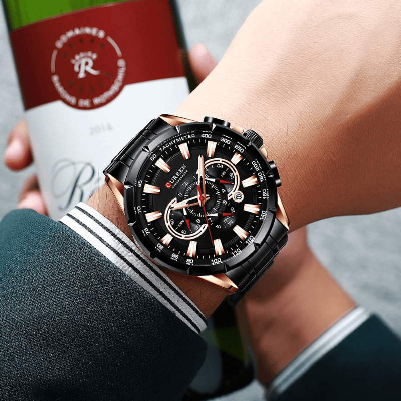 Montre bracelet acier homme noire et or rose au poignet, une bouteille de vin à la main