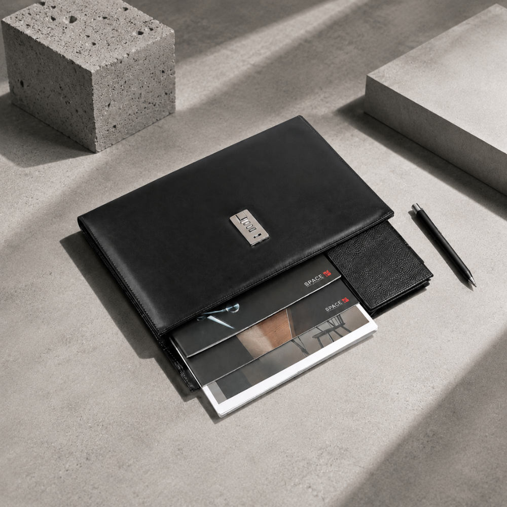 Porte-document noir à code présenté avec magazines, portefeuille et stylo sur béton