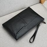 Pochette en cuir noir pour homme posée sur un canapé